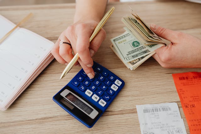 someone using a calculator while holding a wad of cash